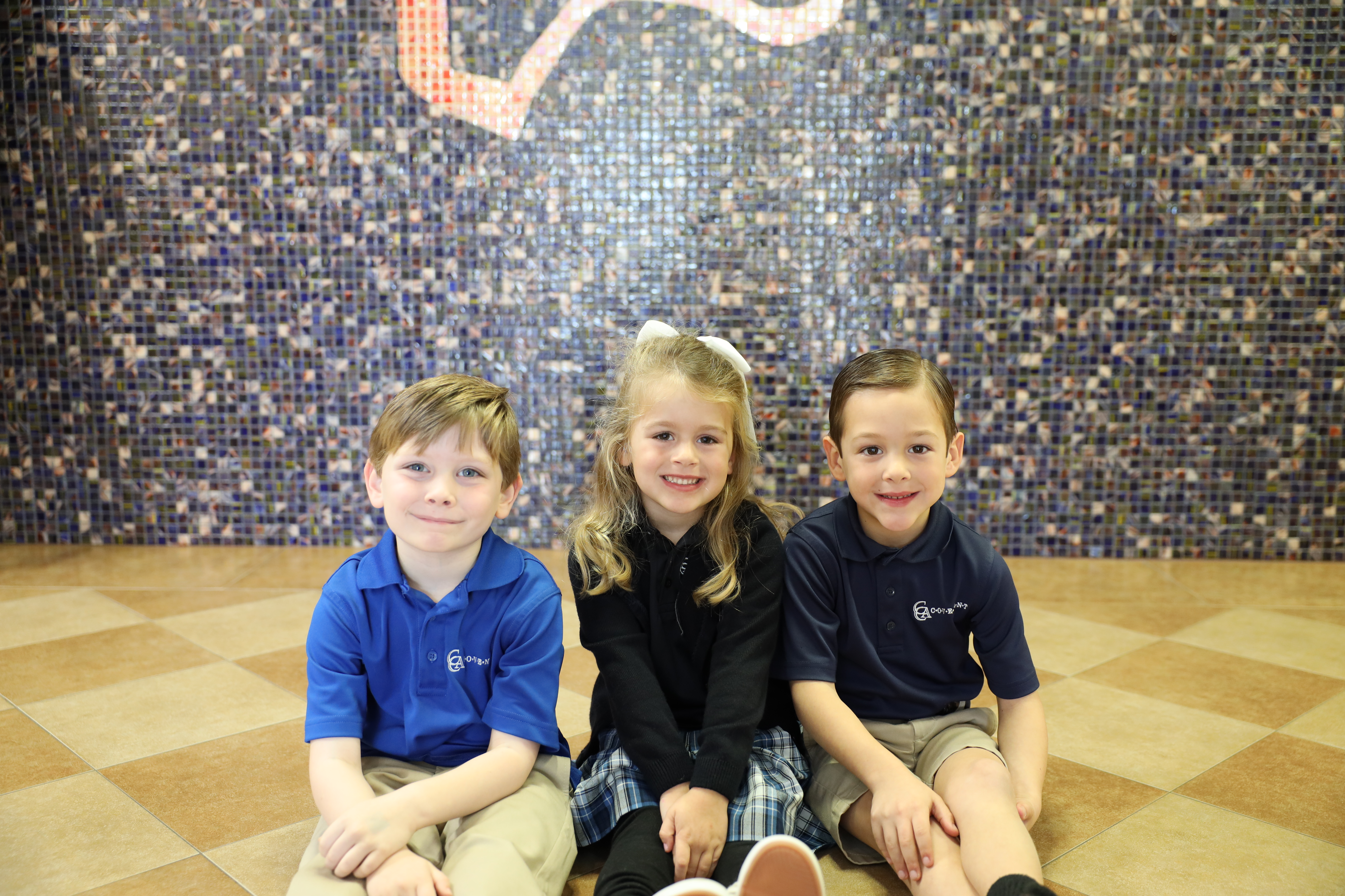 Three young elementary students sitting together smiling 